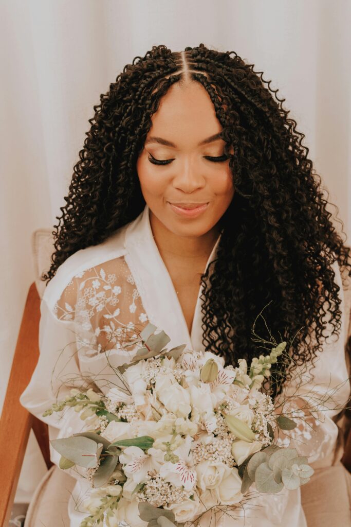 A beautiful bride with curly hair holding a white floral bouquet, exuding elegance and joy.